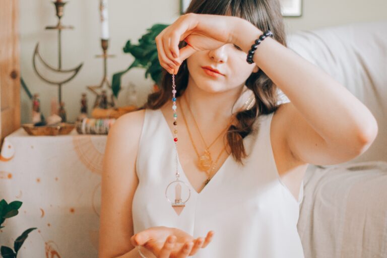 Woman using a crystal pendulum for divination and chakra alignment in a bohemian spiritual setting