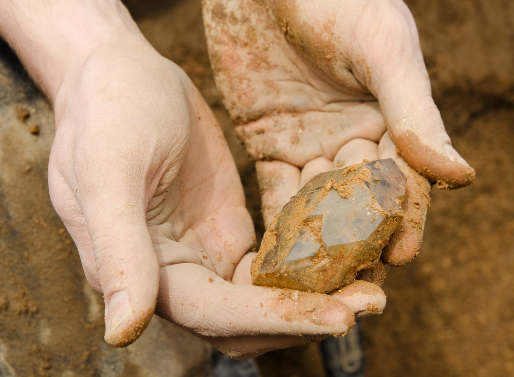 hands holding a raw crystal covered in soil, symbolizing natural earth cleansing