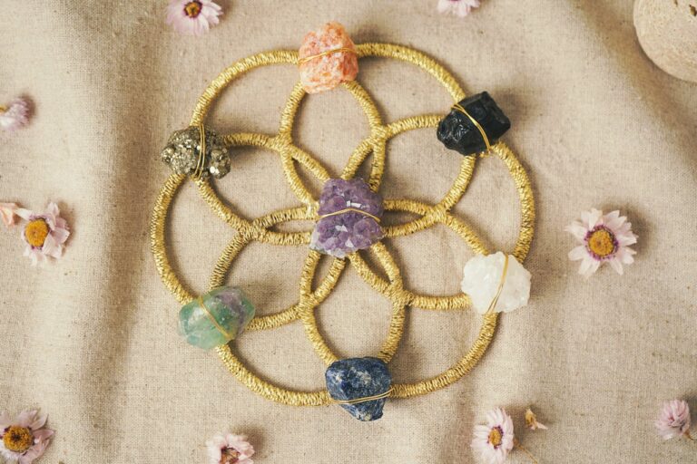 Colorful crystal grid with raw healing stones on a golden Seed of Life pattern, surrounded by dried flowers
