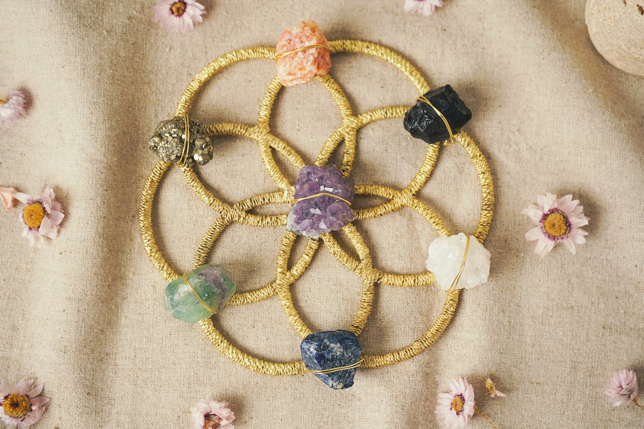 Colorful crystal grid with raw healing stones on a golden Seed of Life pattern, surrounded by dried flowers